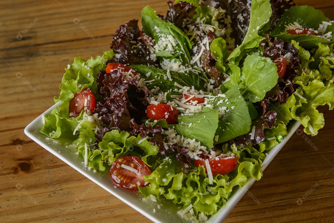 Salada verde em tigela branca na mesa de madeira.