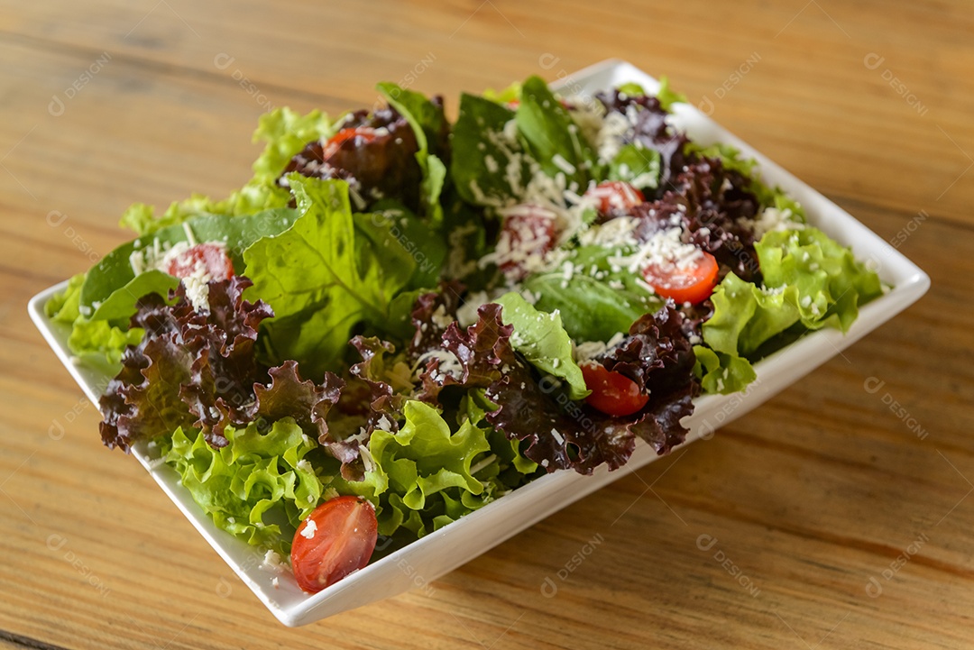 Salada verde em tigela branca na mesa de madeira.