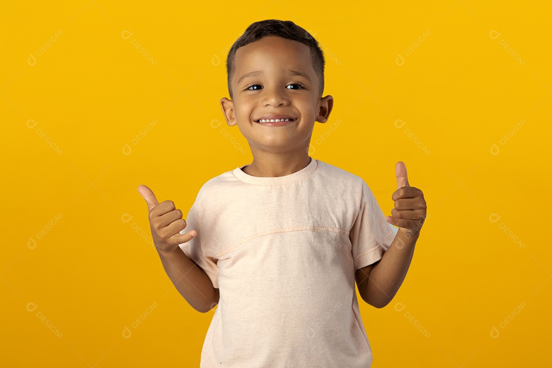 Menino de camisa clara sorrindo com os polegares para comi isolado sobre fundo amarelo