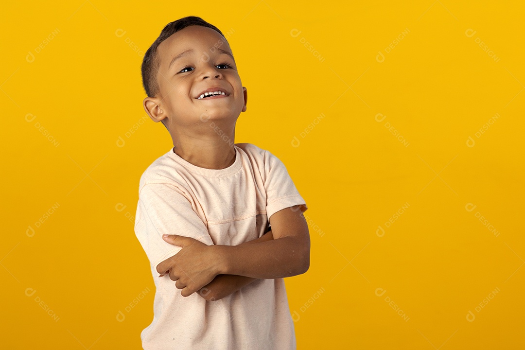 Menino de camisa clara sorrindo e com braços cruzados isolado sobre fundo amarelo