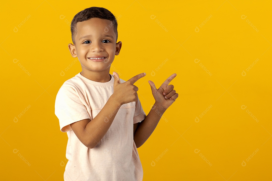 Menino de camisa clara sorrindo apontando para o cima isolado sobre fundo amarelo