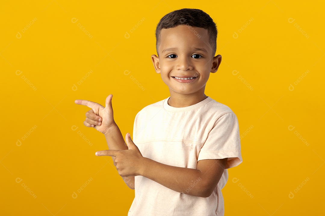 Menino de camisa clara sorrindo apontando para o lado isolado sobre fundo amarelo