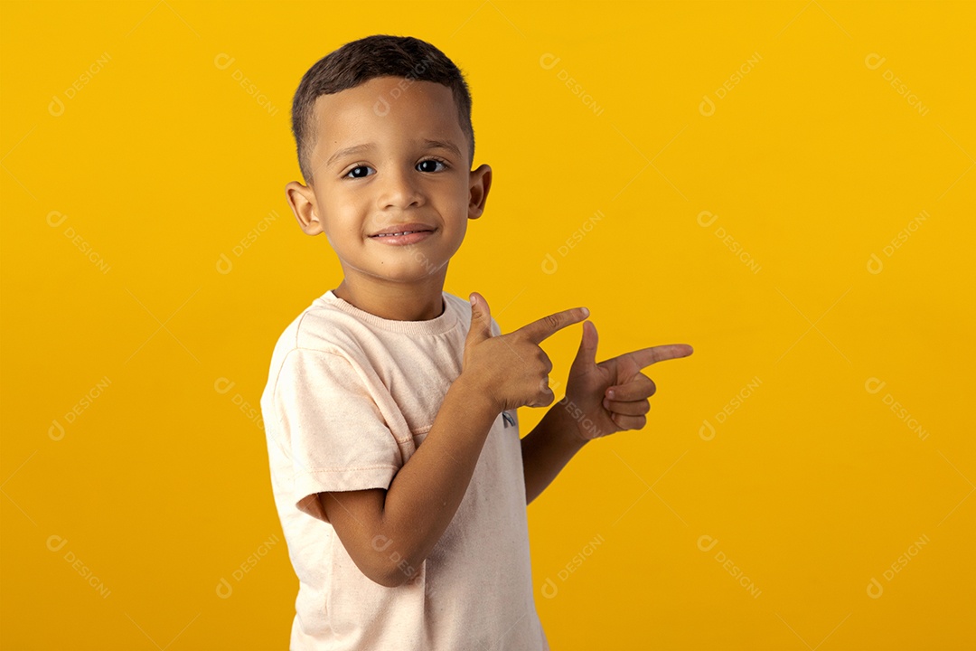 Menino de camiseta cinza apontando para o lado isolado sobre fundo amarelo