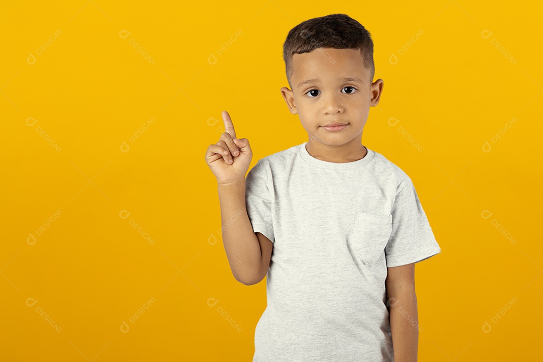 Menino de camiseta cinza apontando para cima isolado sobre fundo amarelo