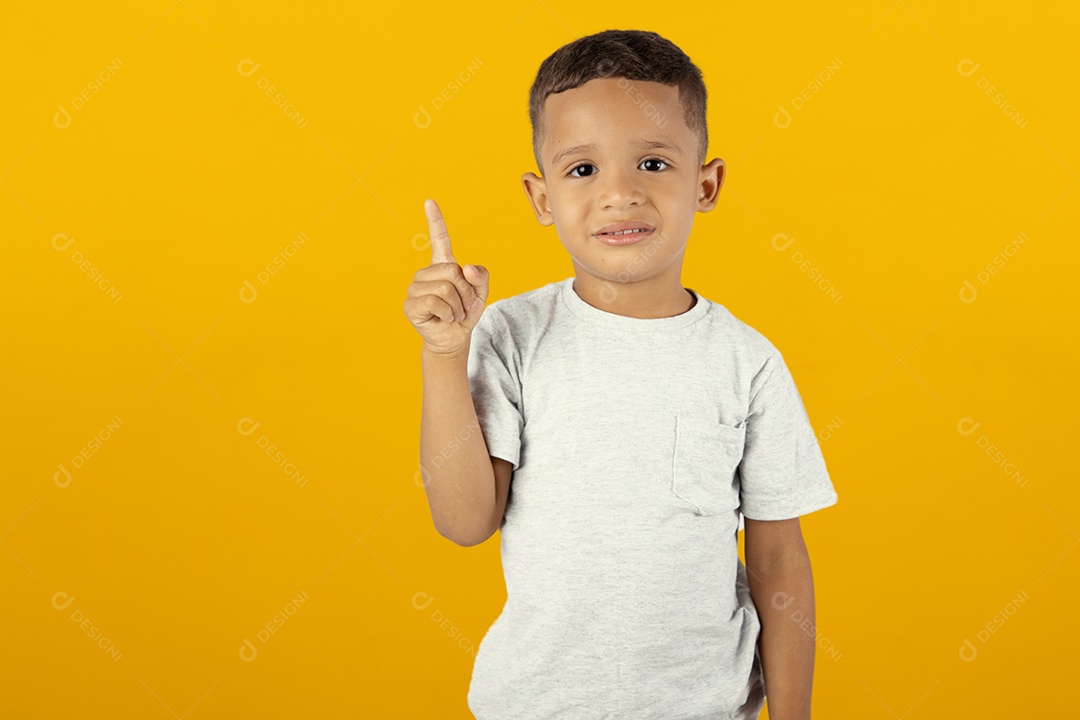 Menino de camiseta cinza apontando para cima isolado sobre fundo amarelo