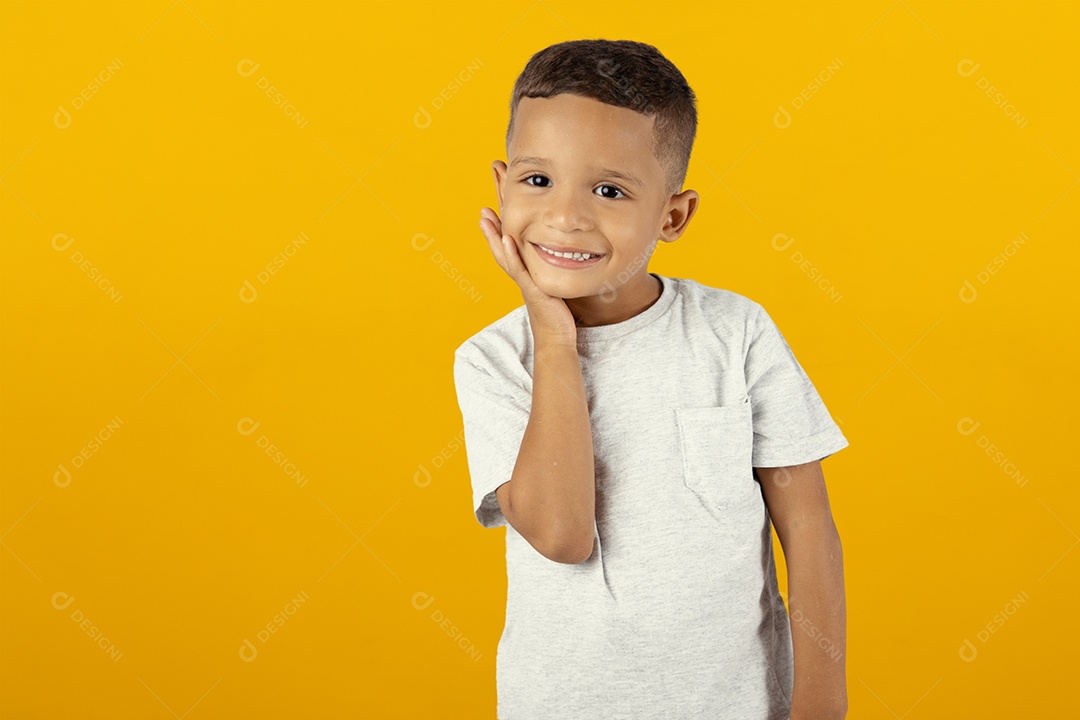 Menino feliz tocando sua maçã do rosto isolado sobre fundo amarelo