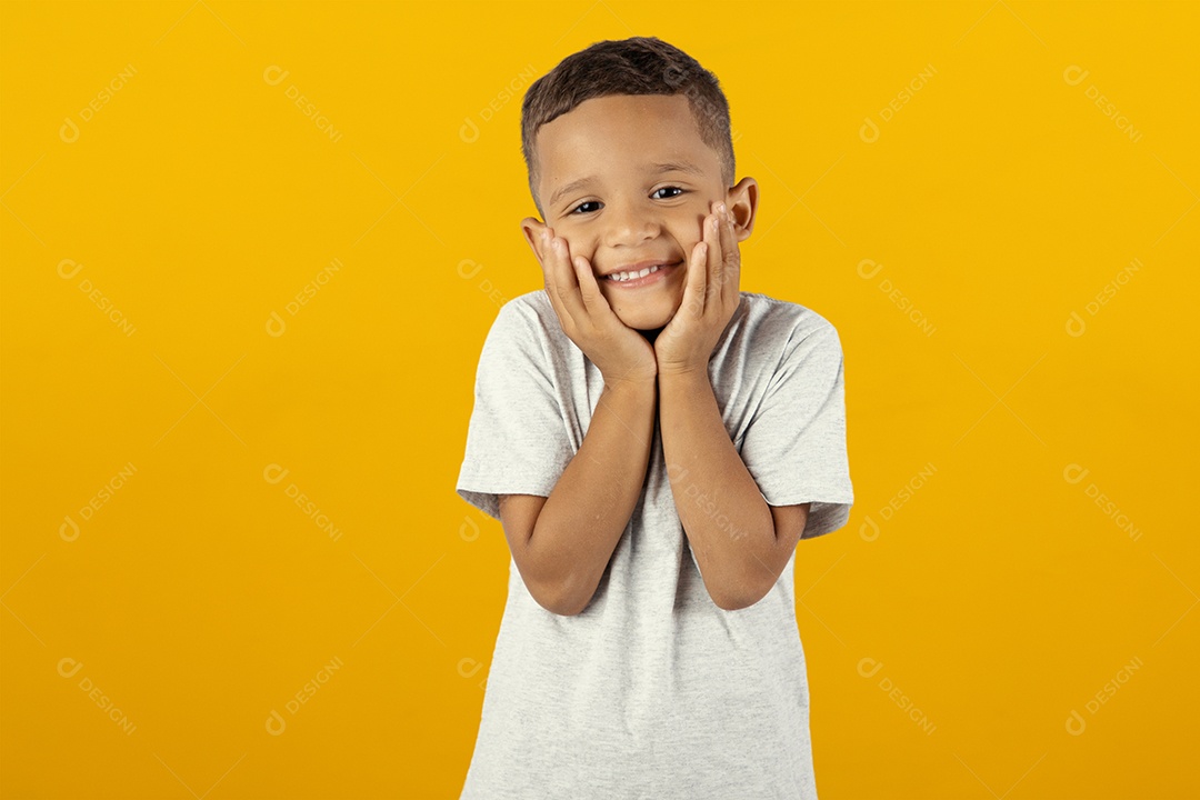 Menino feliz moreno tocando as maçãs do rosto com as mãos sobre fundo amarelo