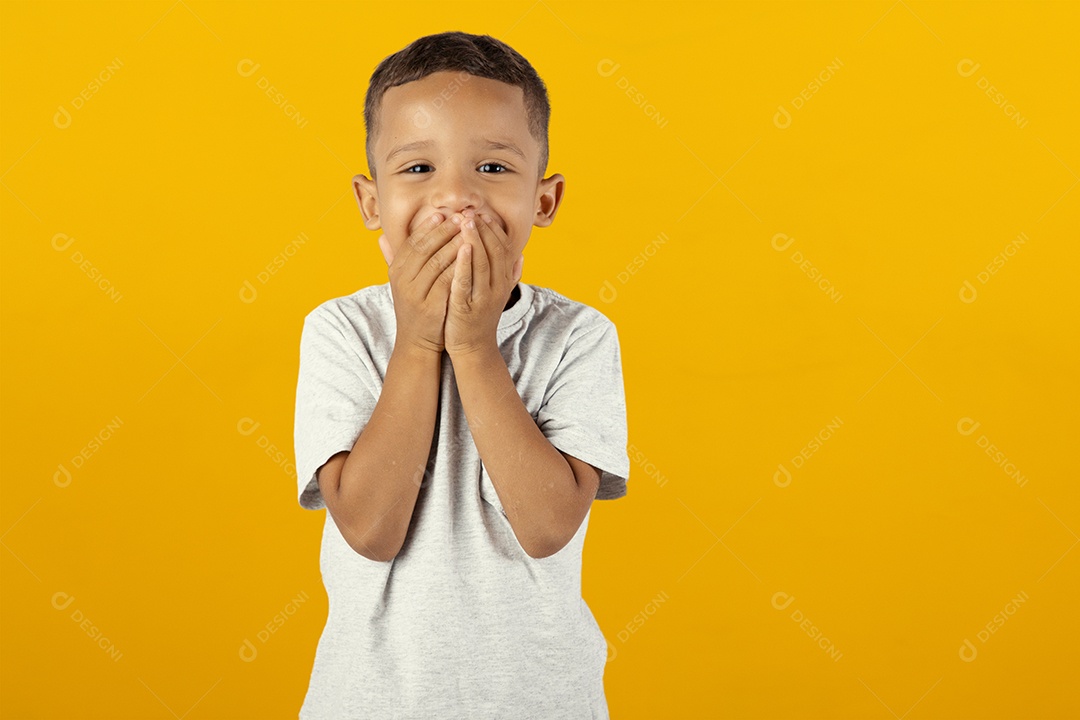 Menino de camisa cinza alegre com mãos na boca isolado sobre fundo amarelo