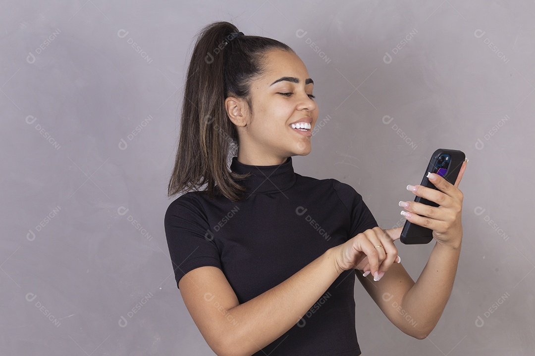 Mulher jovem sorridente com cabelo preso segurando um smartphone celular