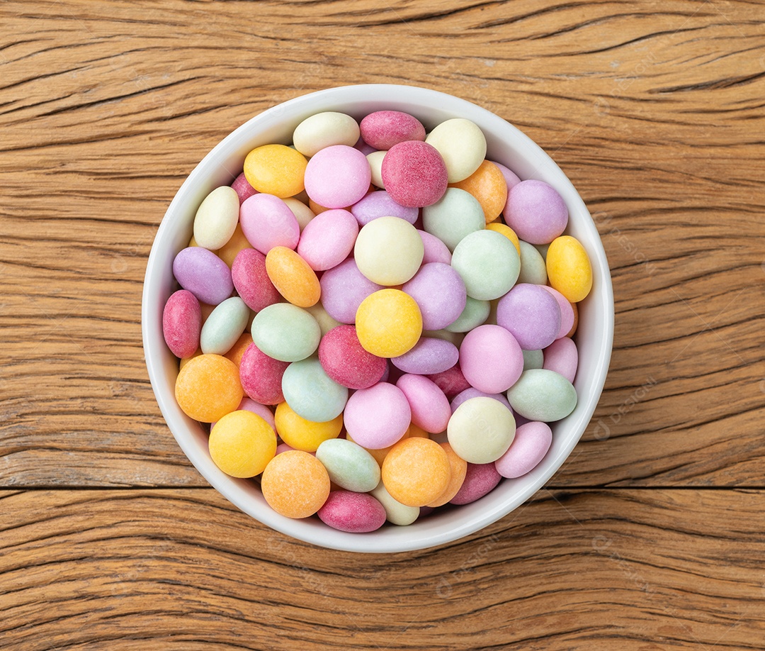 Doces coloridos em uma tigela sobre a mesa de madeira.