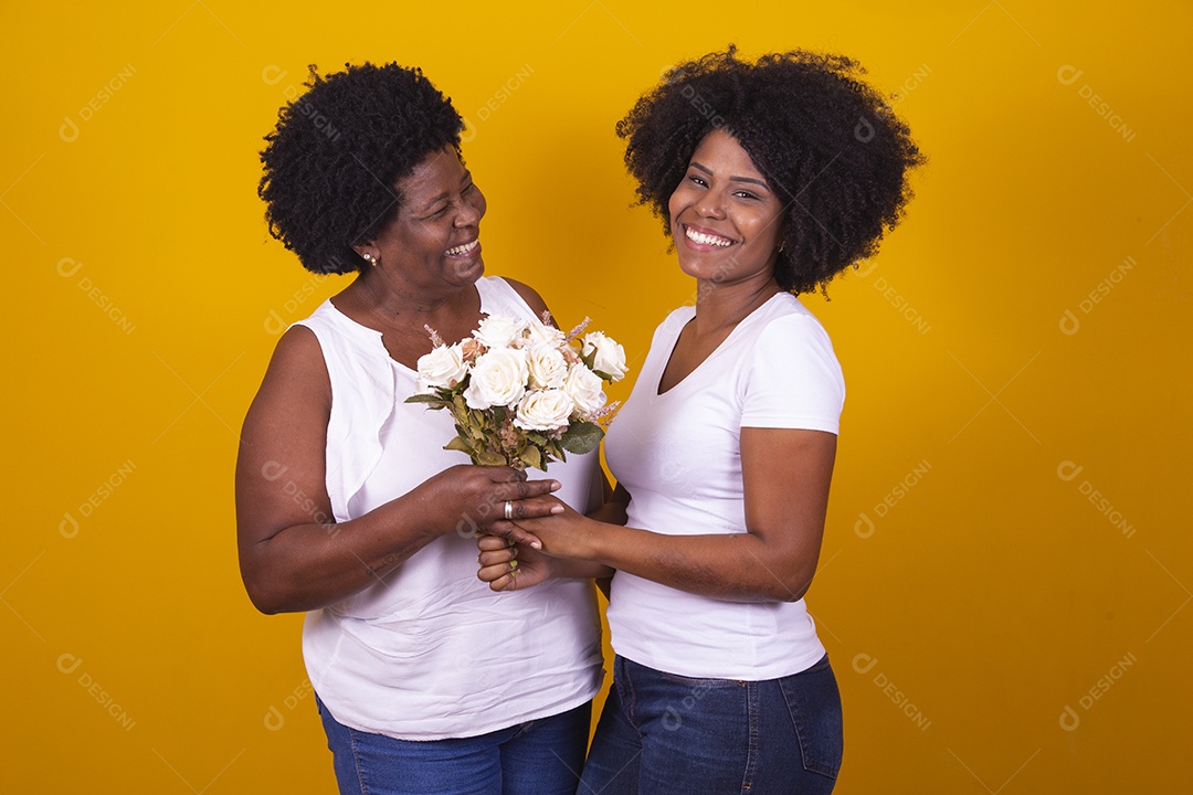 Mulheres negras mãe e filha vestidas com blusa branca com gestos de carinho segurando buque de flores