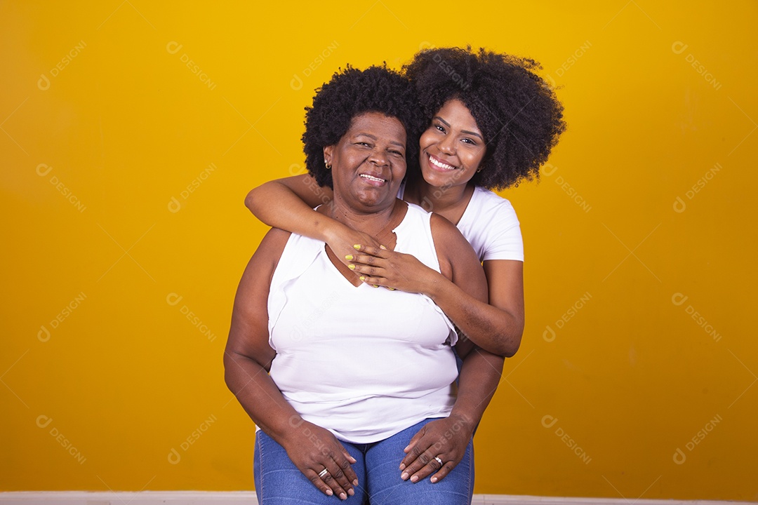 Mulheres negras mãe e filha vestidas com blusa branca abraçadas