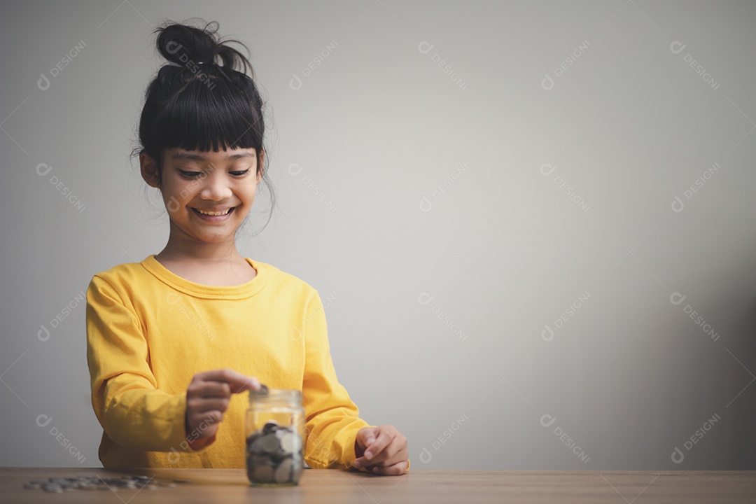 Menina asiática bonitinha fazendo pilhas de moedas. Criança salva