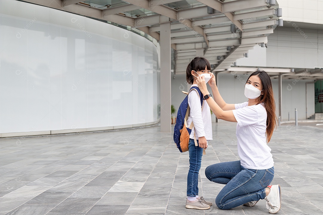 Mãe asiática ajuda sua filha usando uma máscara médica para proteção