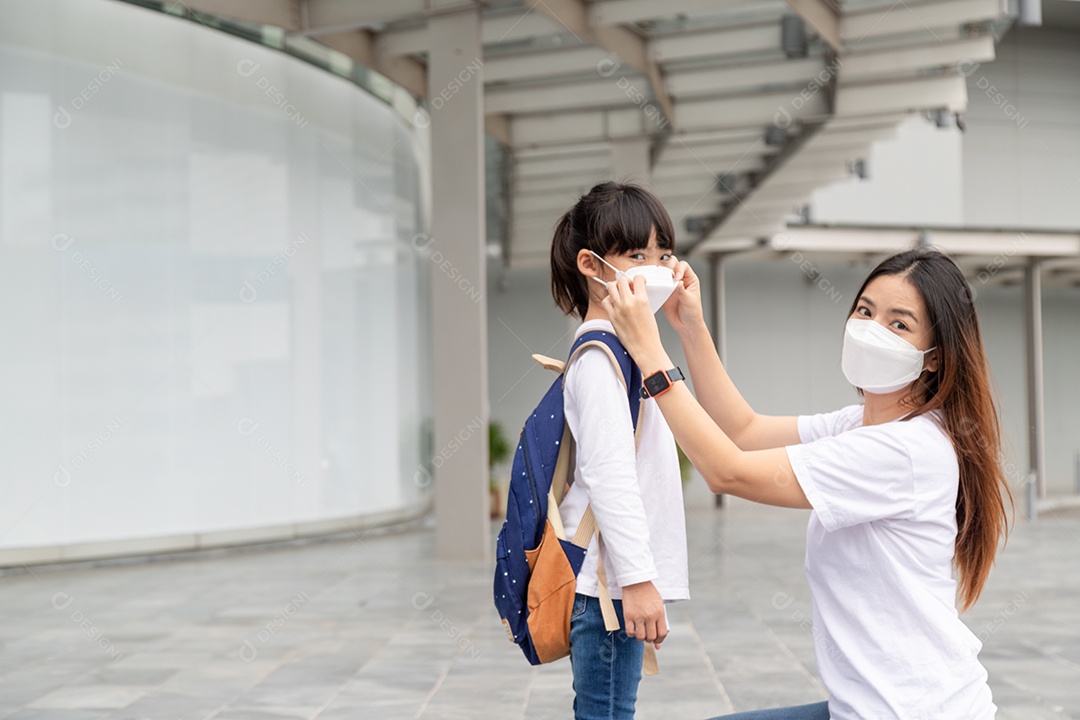 Mãe asiática ajuda sua filha usando uma máscara médica para proteção