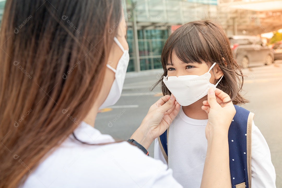 Mãe asiática ajuda sua filha usando uma máscara médica para proteção