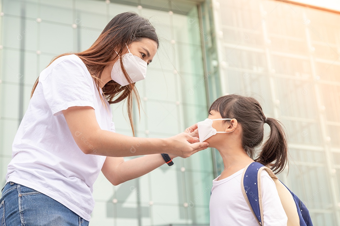 Mãe asiática ajuda sua filha usando uma máscara médica para proteção