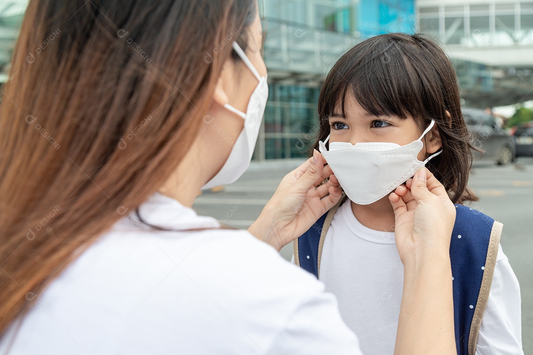 Mãe asiática ajuda sua filha usando uma máscara médica para proteção