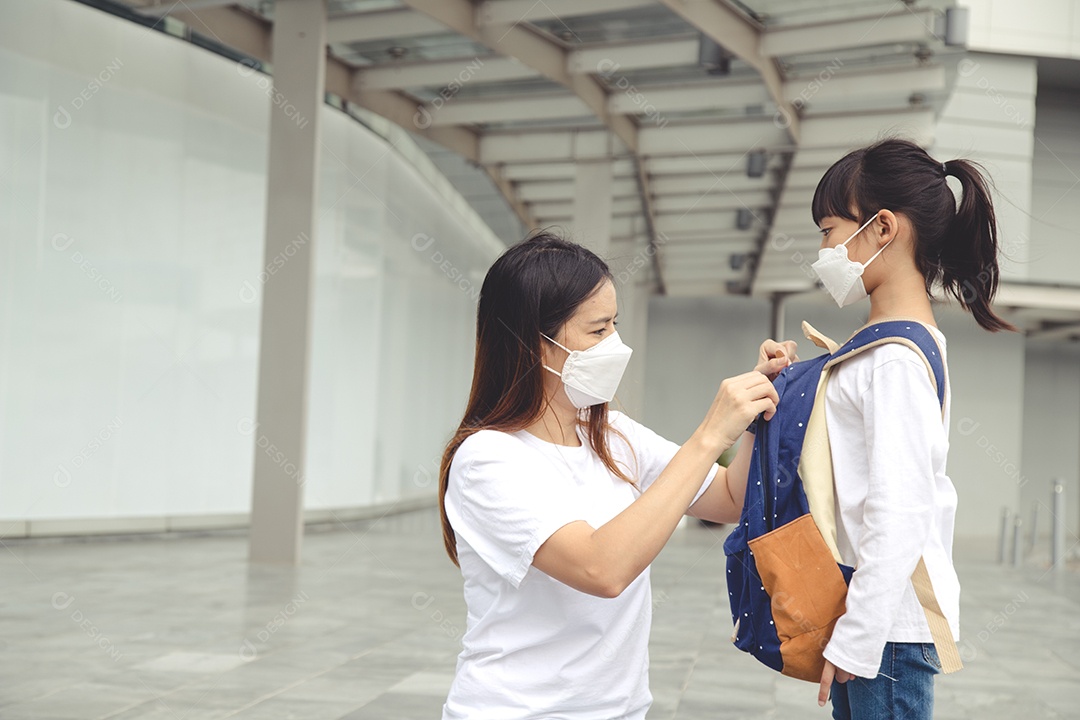 Mãe asiática ajuda sua filha usando uma máscara médica para proteção