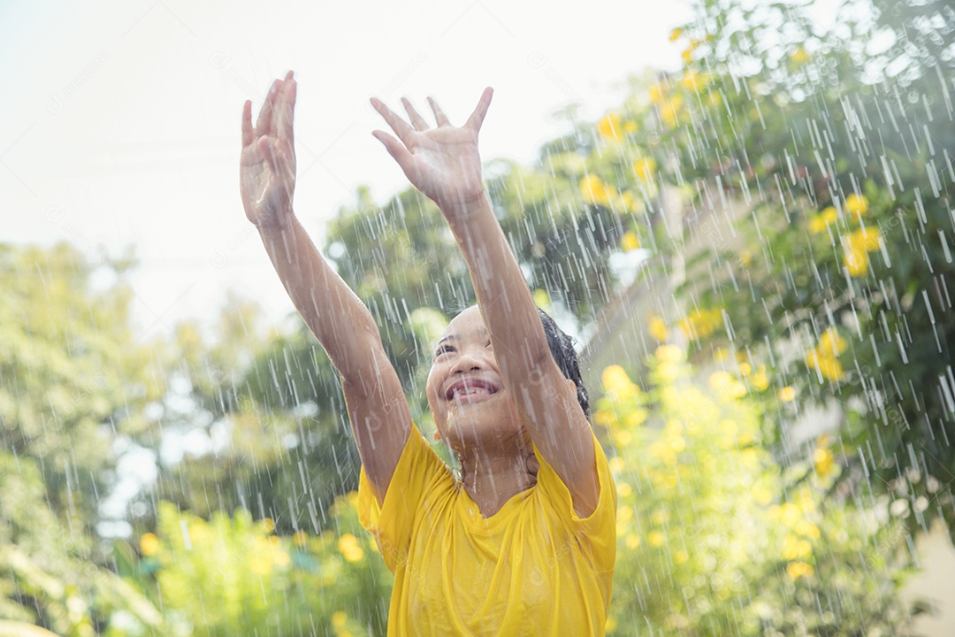 Feliz garotinha asiática se divertindo para brincar com a chuva à luz do sol