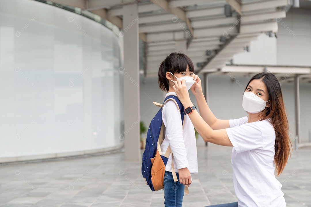 Mãe asiática ajuda sua filha usando uma máscara médica para proteção