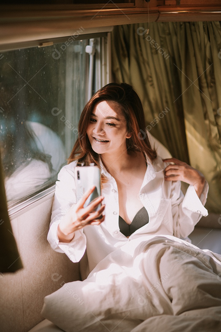 Mulher bonita sexy com um smartphone na cama