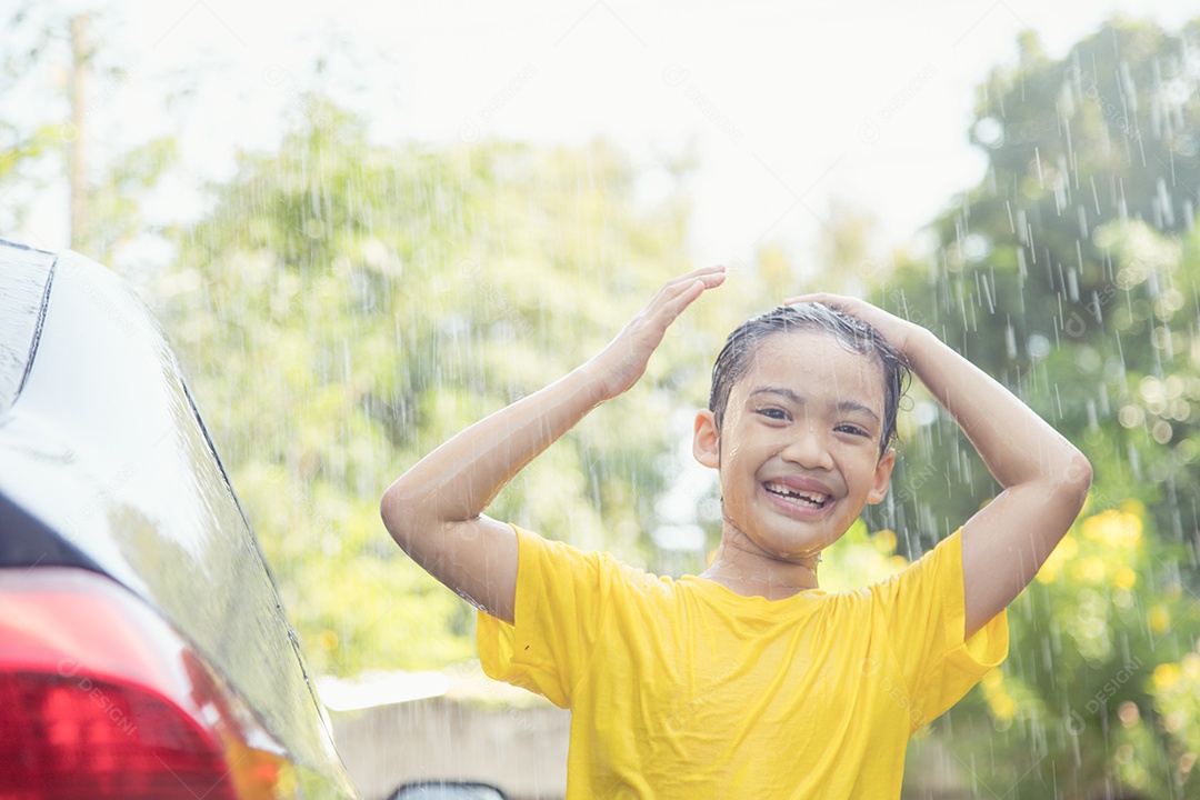 Menina asiática feliz lavando carro em salpicos de água e luz solar em casa