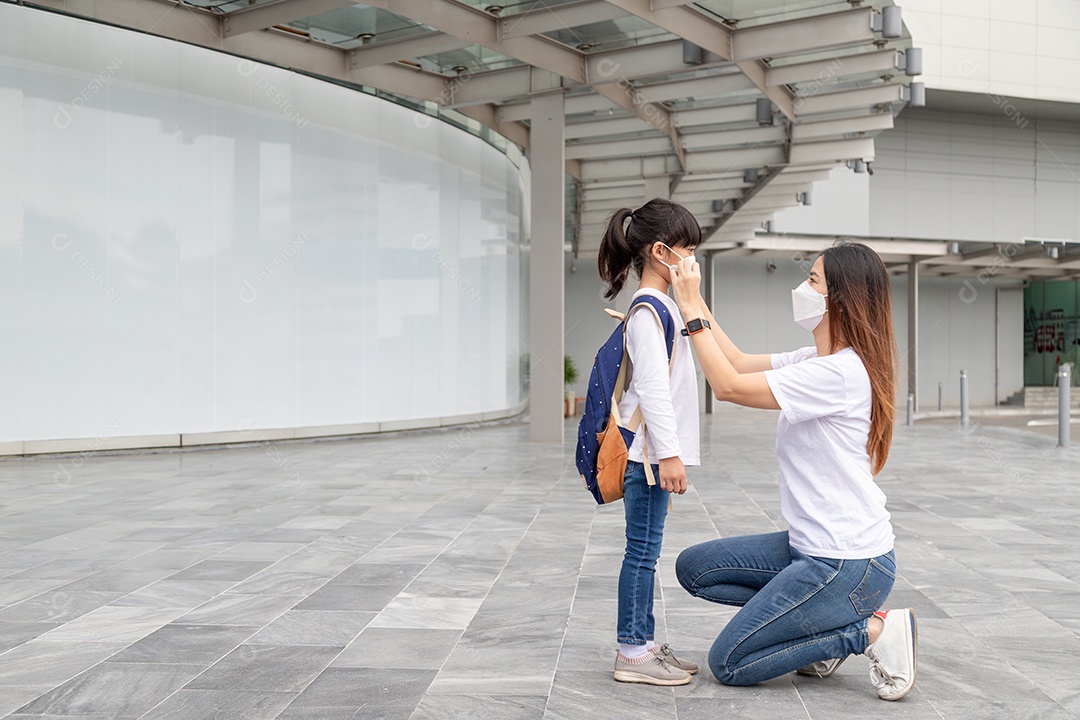 Mãe asiática ajuda sua filha usando uma máscara médica para proteção