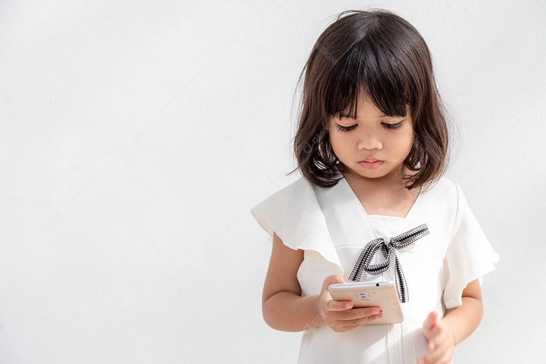 Uma garotinha está concentrada no telefone, olhe para o smartphone