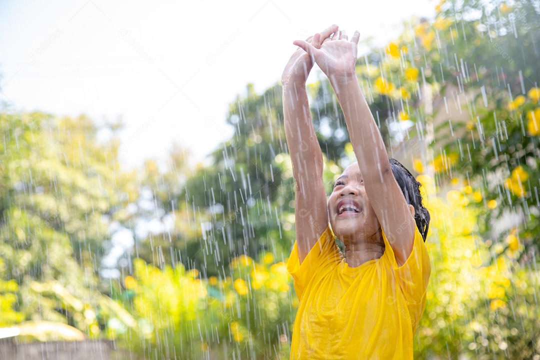 Feliz garotinha asiática se divertindo para brincar com a chuva à luz do sol