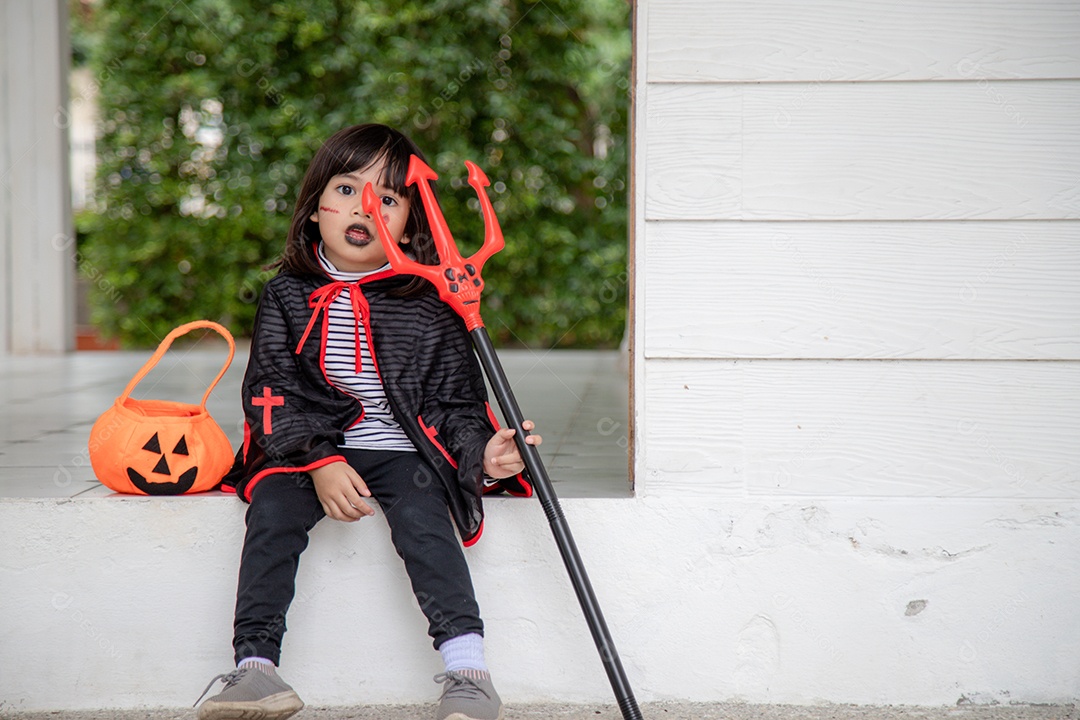 Menina asiática em fantasia de demônio segurando tridente preto e vermelho