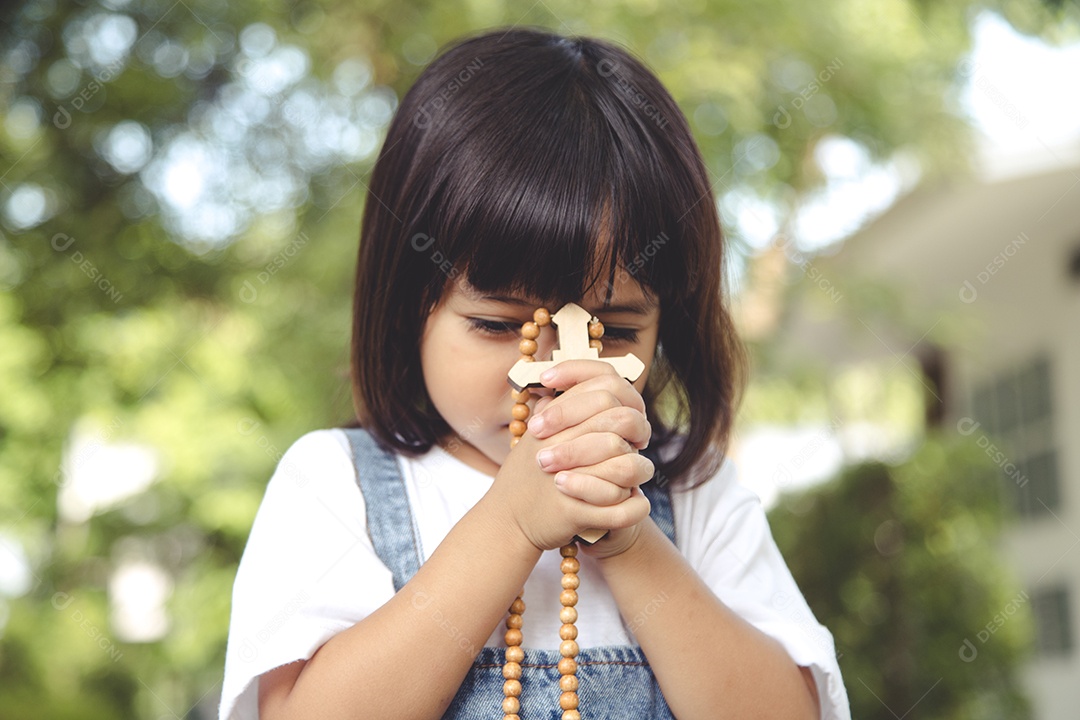 Menina asiática rezando segurando a cruz, conceito cristão.