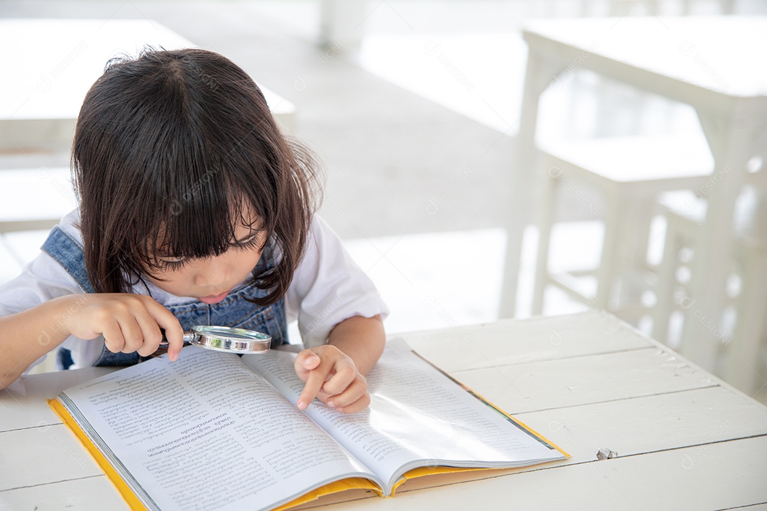 Menina asiática lendo os livros na mesa com uma lupa