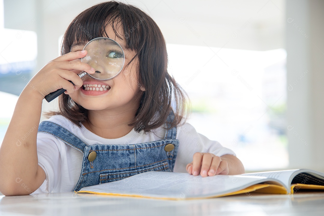 Menina asiática lendo os livros na mesa com uma lupa