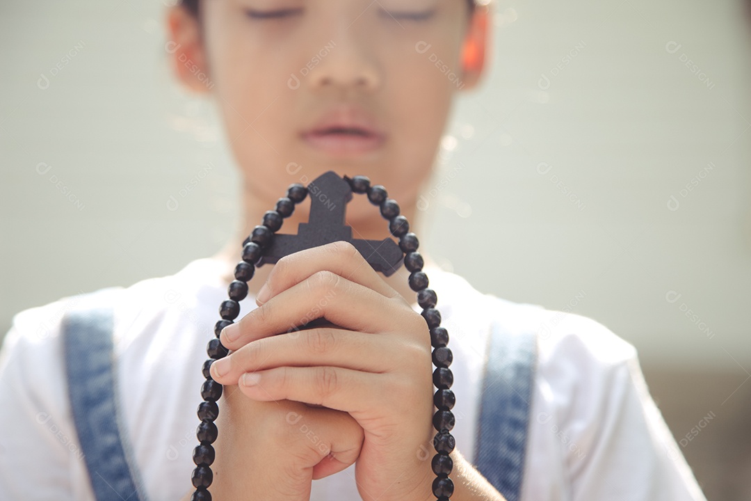 Menina asiática rezando segurando a cruz, conceito cristão.