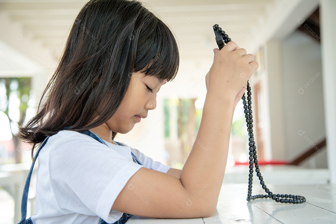 Menina asiática rezando segurando a cruz, conceito cristão.