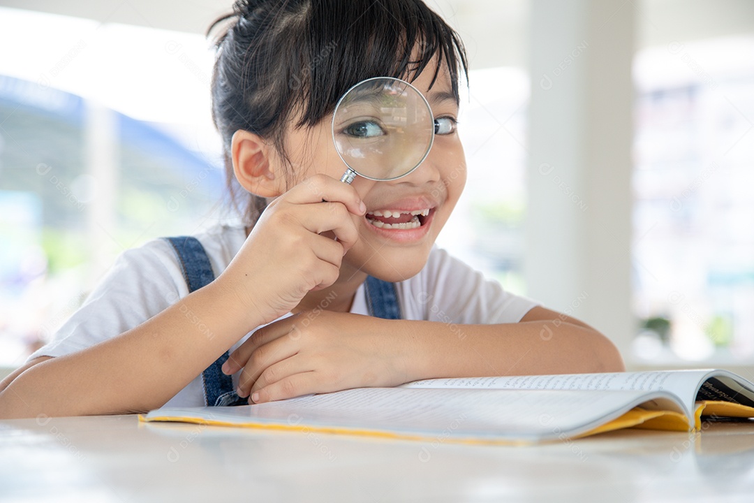 Menina asiática lendo os livros na mesa com uma lupa