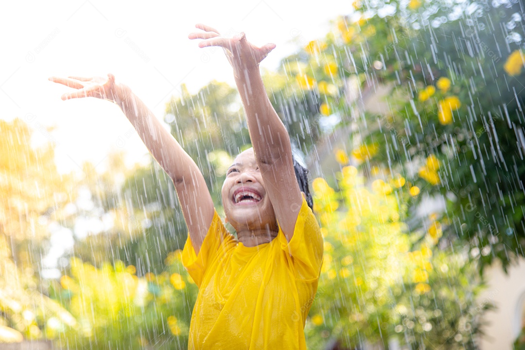 Feliz garotinha asiática se divertindo para brincar com a chuva à luz do sol