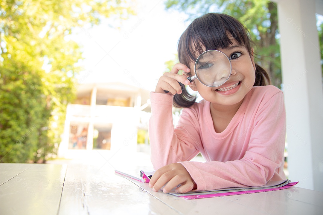 Menina asiática lendo os livros na mesa com uma lupa