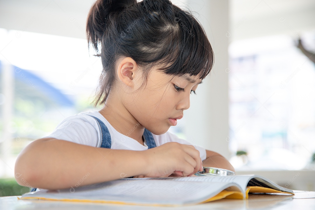 Menina asiática lendo os livros na mesa com uma lupa
