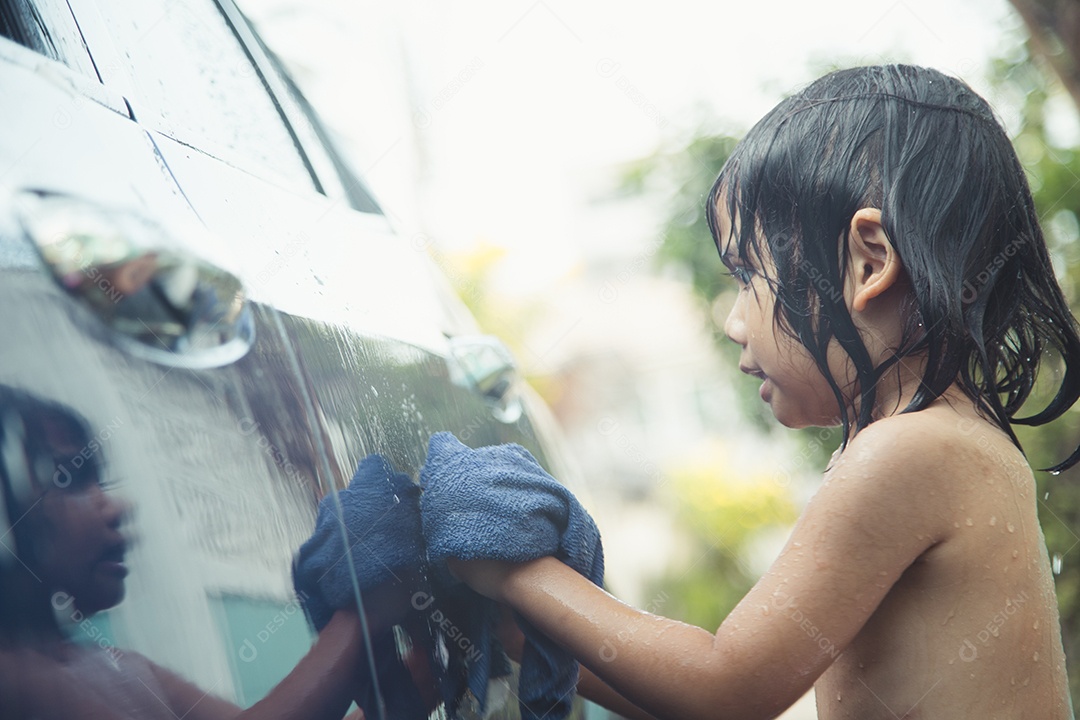 Linda criança asiática lavando um carro com mangueira no dia de verão