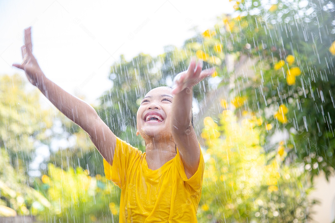 Feliz garotinha asiática se divertindo para brincar com a chuva à luz do sol