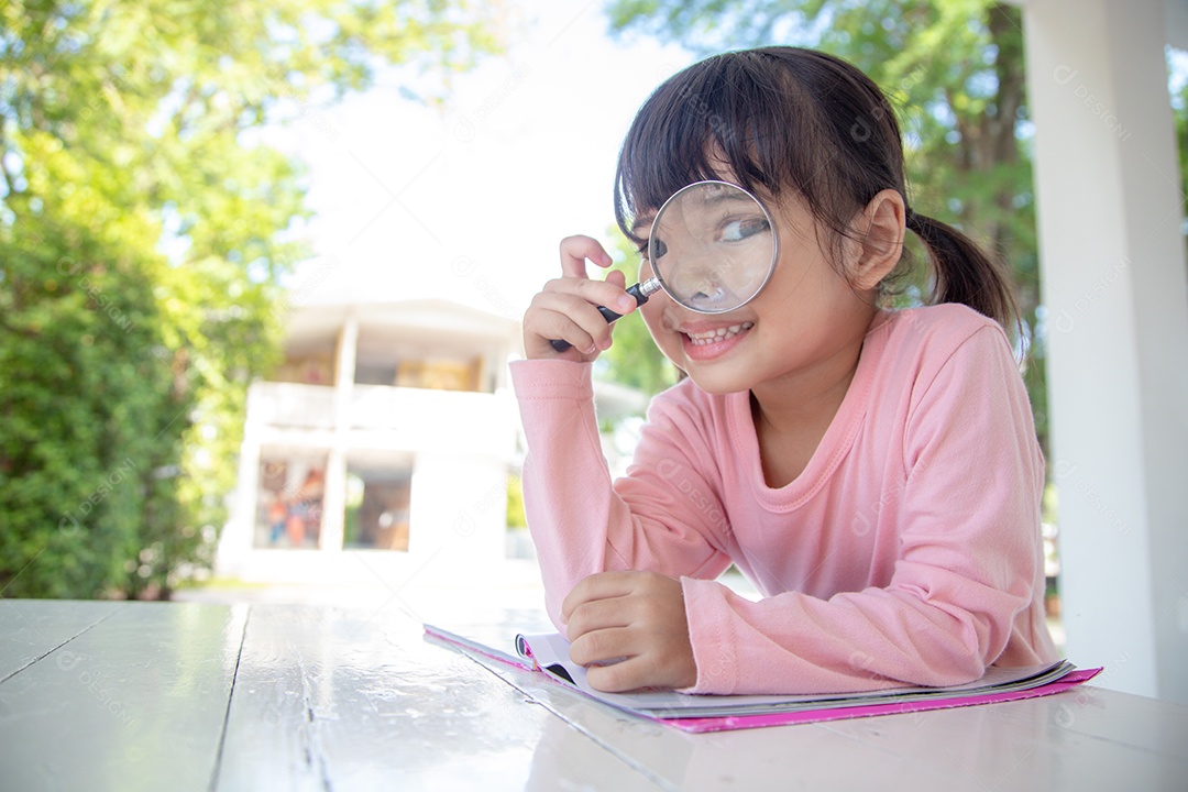 Menina asiática lendo os livros na mesa com uma lupa