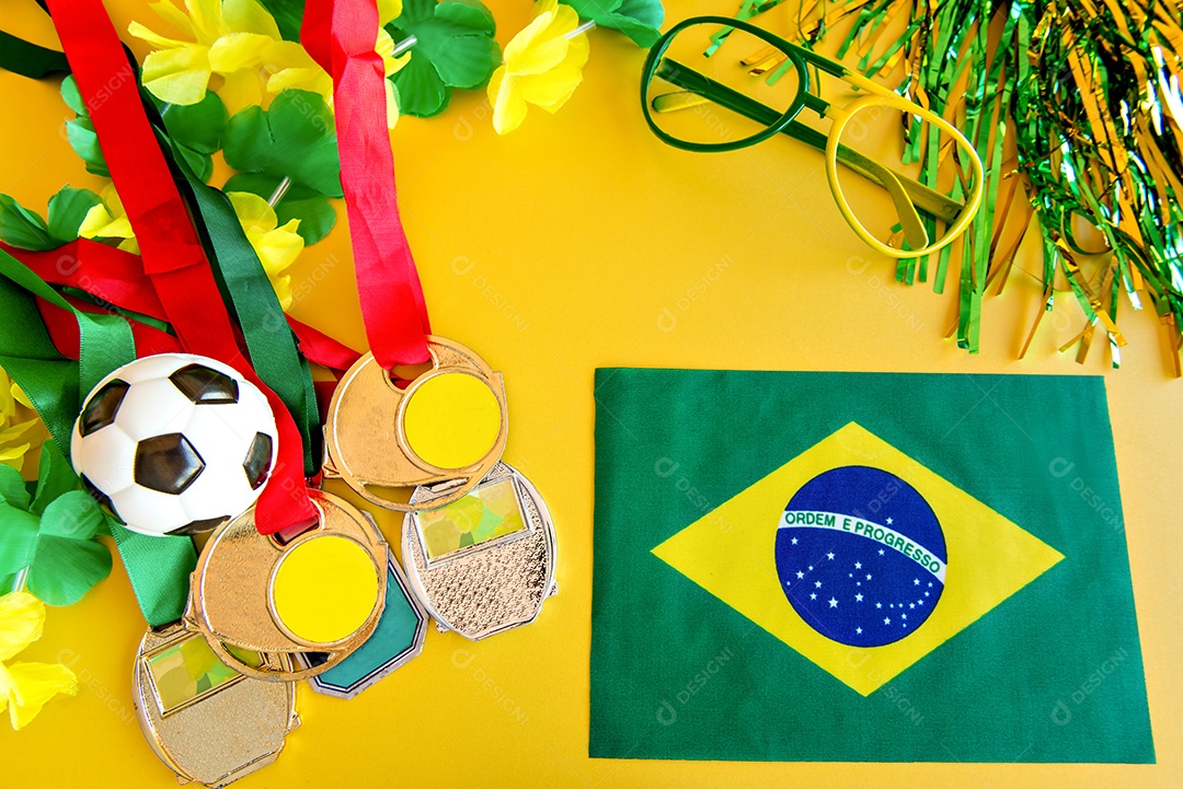 Bola de futebol, medalhas e bandeira brasileira em fundo amarelo