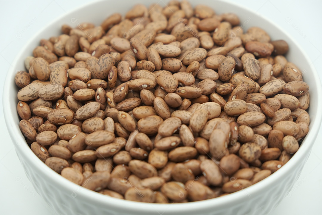 Feijão cru em tigela branca na mesa branca.