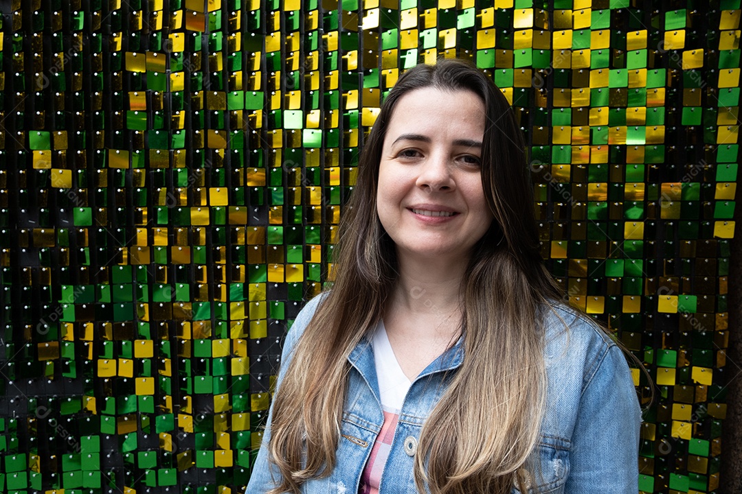 Mulher morena sorrindo na frente de um bac verde e amarelo brilhante.