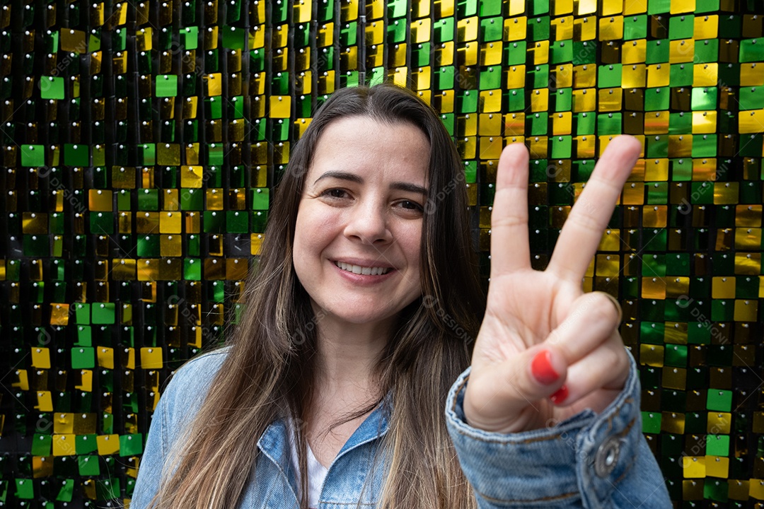 Mulher morena sorrindo na frente de glitter verde e amarelo de volta.