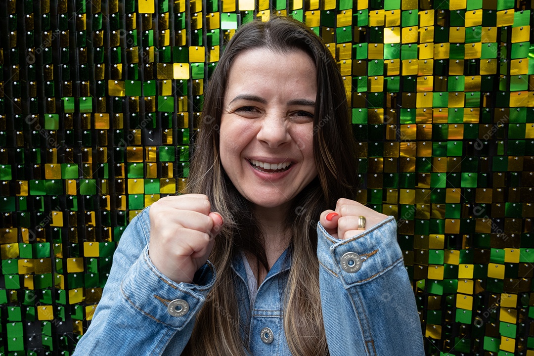 Mulher morena sorrindo e torcendo com as mãos na frente.