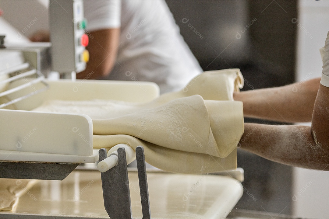 People working in a bakery passing dough through the cylinder