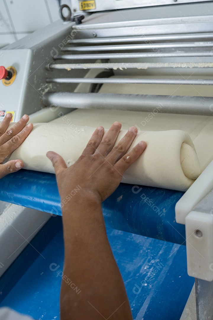 Pessoas trabalhando em uma padaria, passando massa pelo cilindro